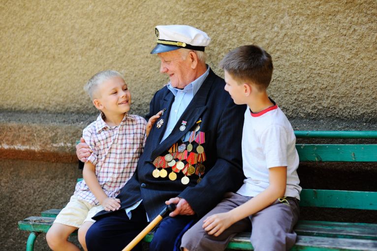 WWII veteran with children. Grandchildren looking at grandfather's military awards.