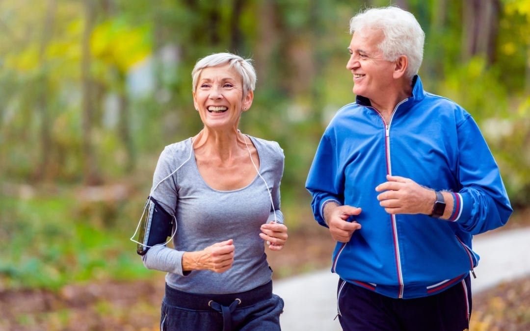 Elderly couple jogging through the woods while chatting and laughing